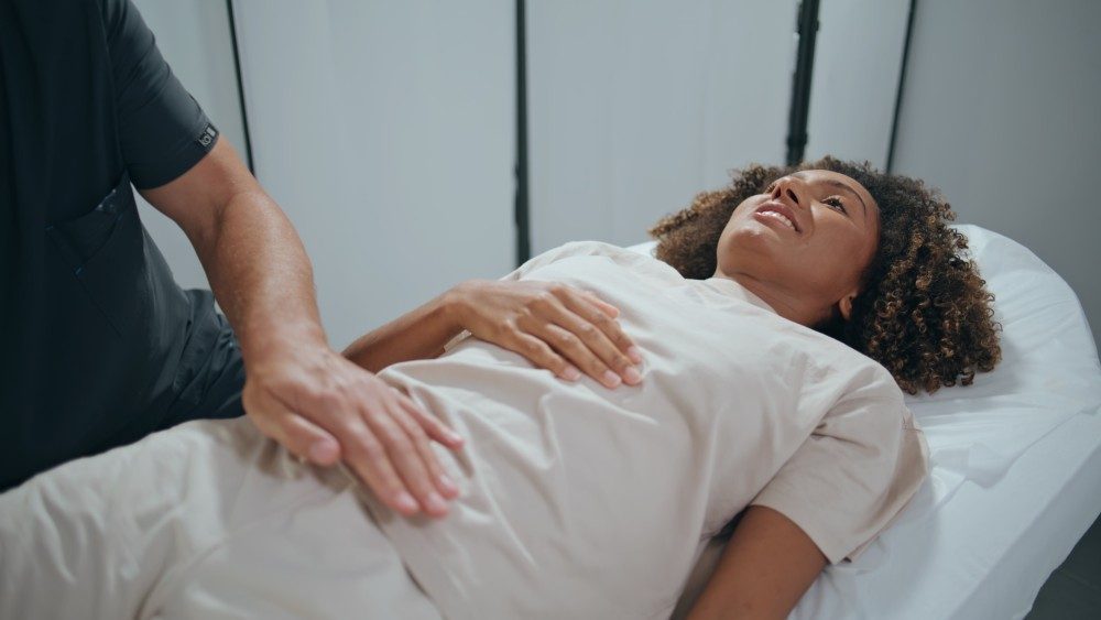 A woman lying on an exam table while a clinician gently examines her lower abdomen