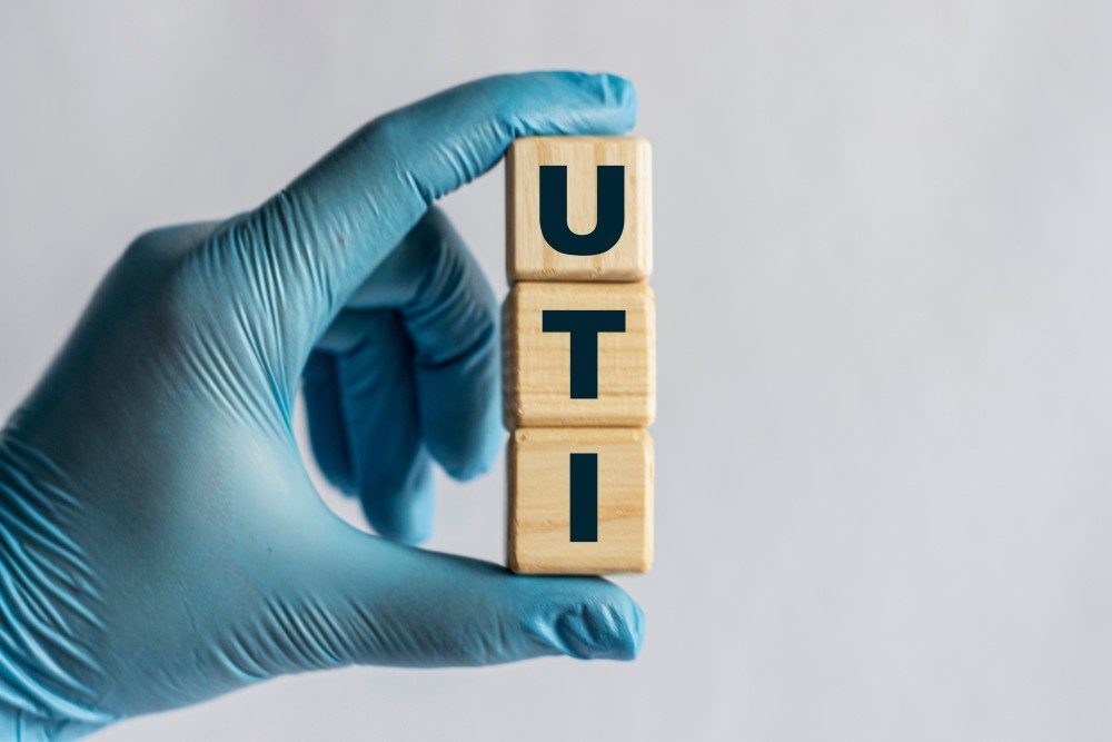 A gloved hand holding wooden blocks that spell UTI