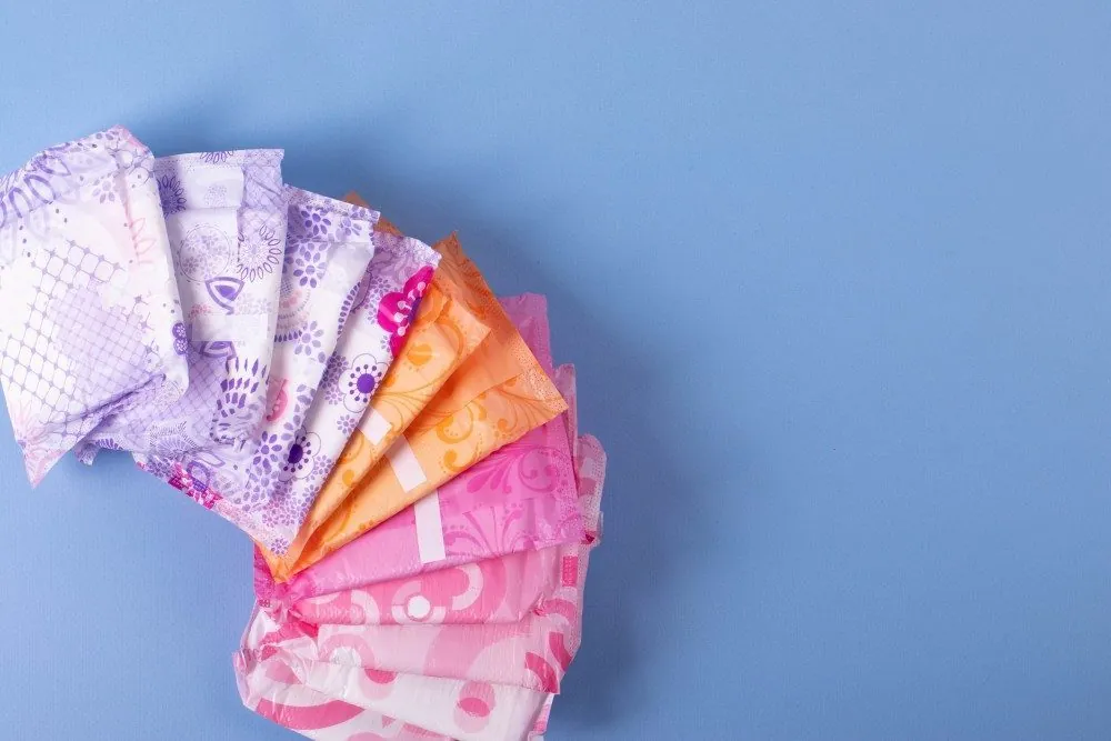 A fan of pads, liners and tampons in colorful wrappers on a blue background