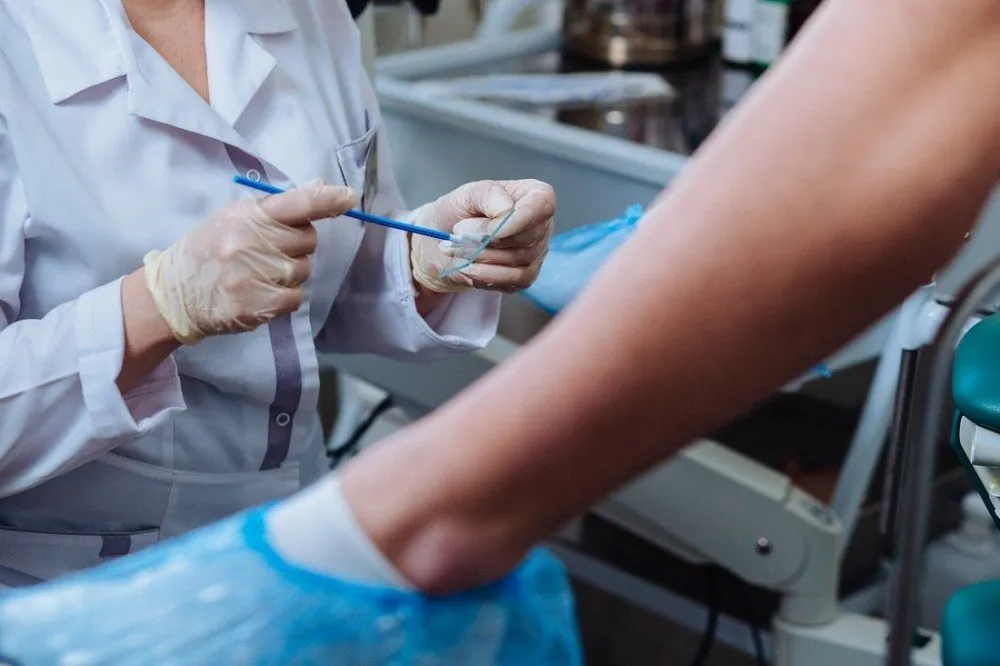A clinician's gloved hands holding a cervical sampling brush