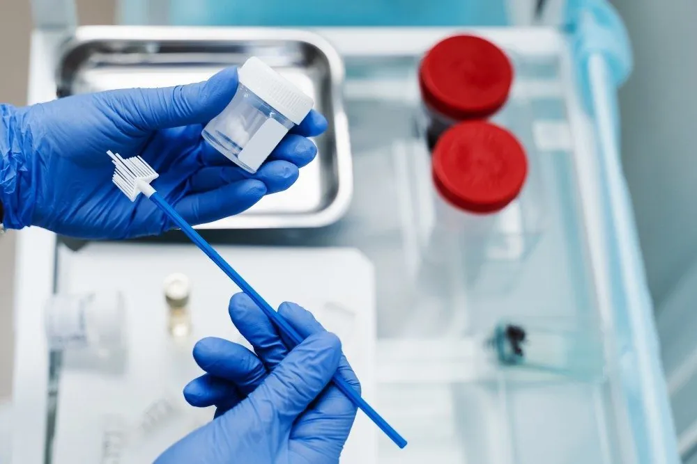 A gloved hand placing a sampling brush into a liquid-based Pap vial
