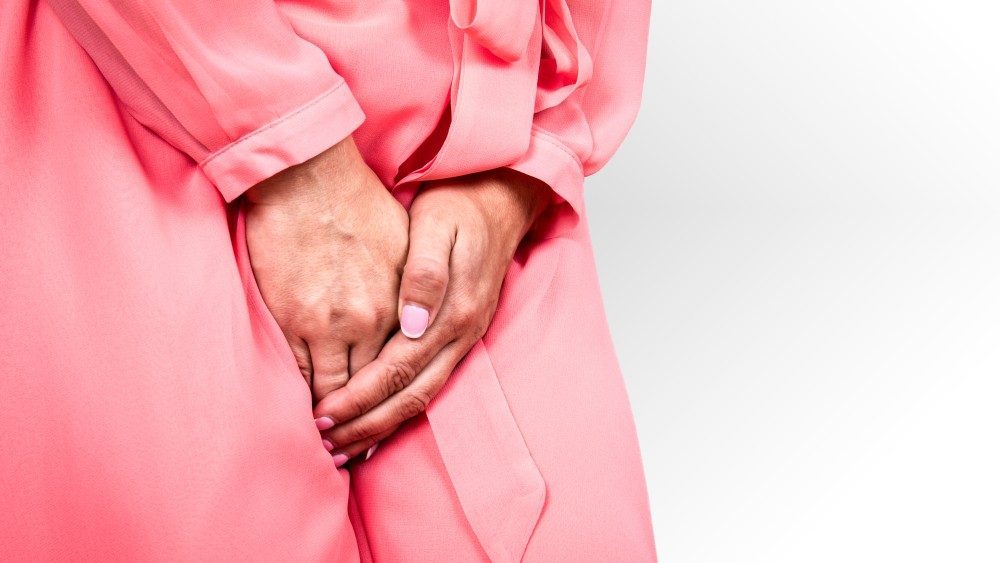 A woman in a pink robe holding her hands over her lower abdomen