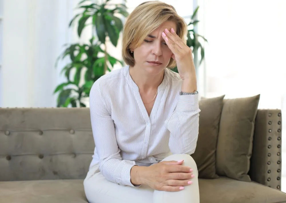 A woman in her fifties on a sofa with her hand to her forehead