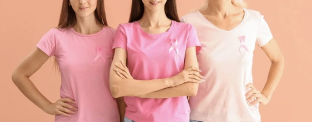 Three women in pink shirts with pink ribbons, arms linked