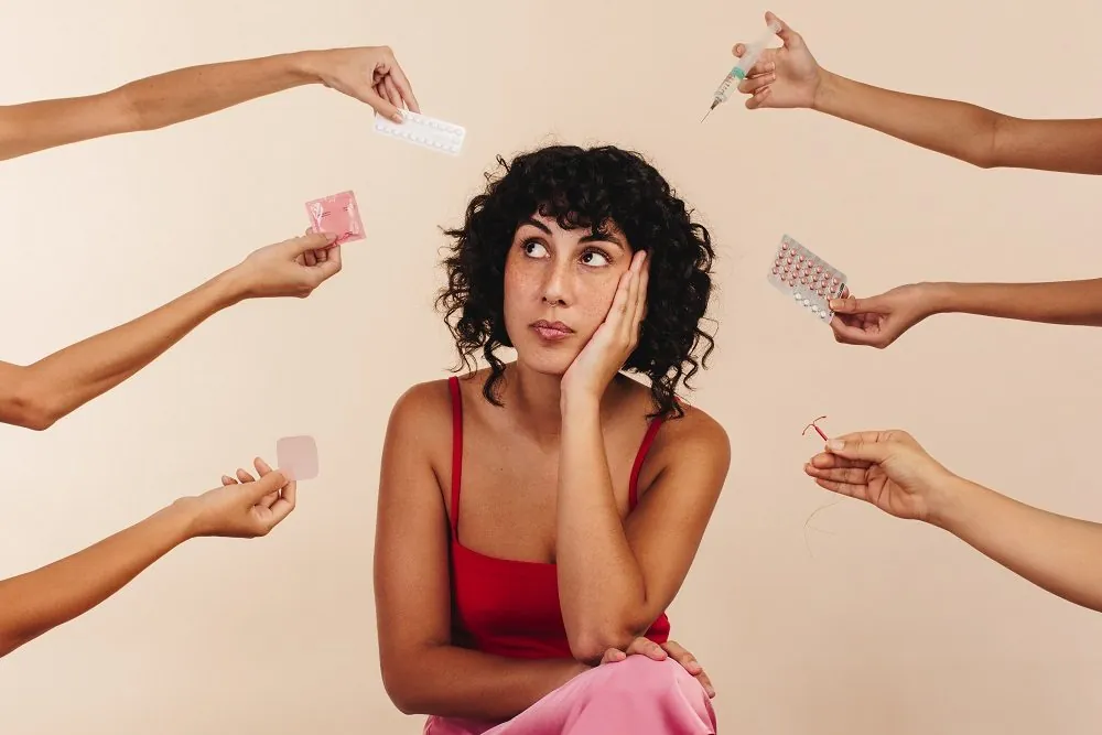 A woman choosing between contraceptive options held out to her: pills, a ring, a patch and condoms