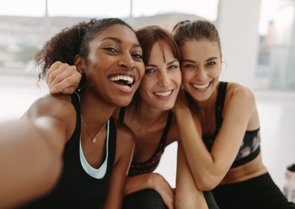 Three friends in workout clothes smiling together after exercise