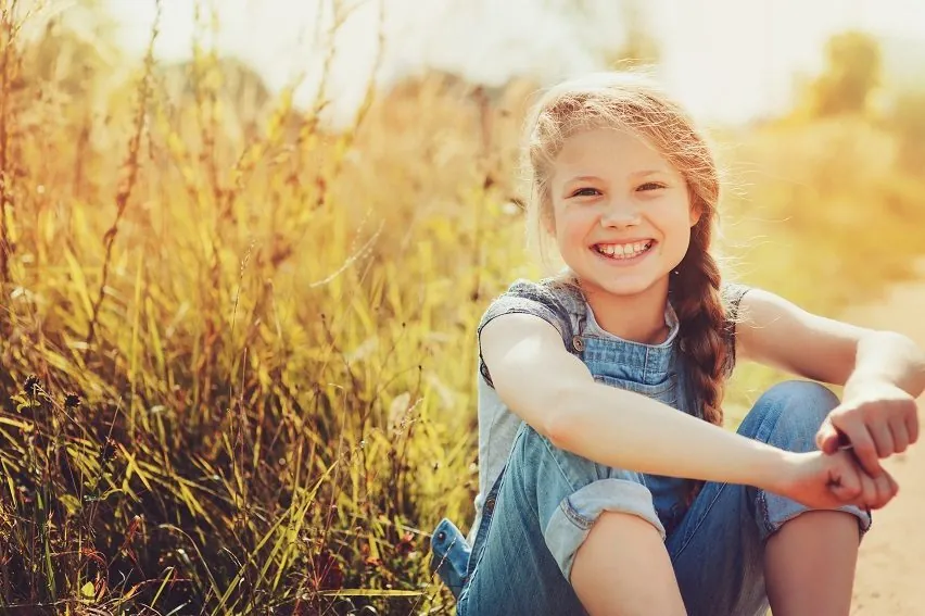 A young girl in overalls smiling in a sunny field