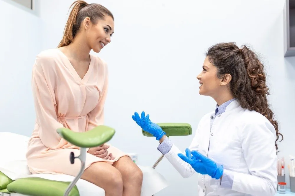 A gynecologist in gloves talking with a patient in a pink gown