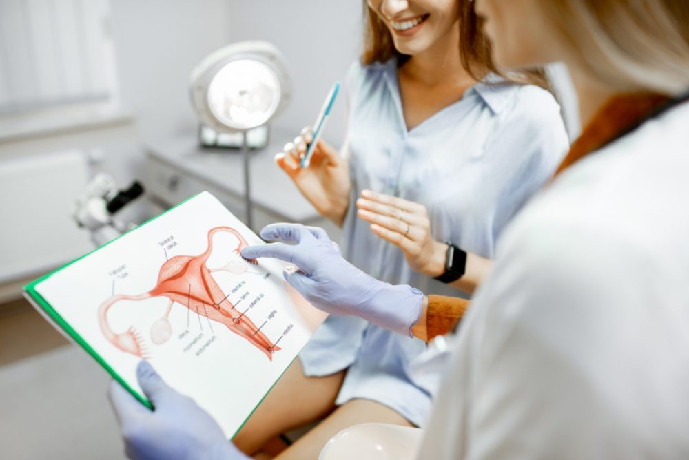 A gynecologist pointing to a diagram of the uterus on a tablet while talking with a patient