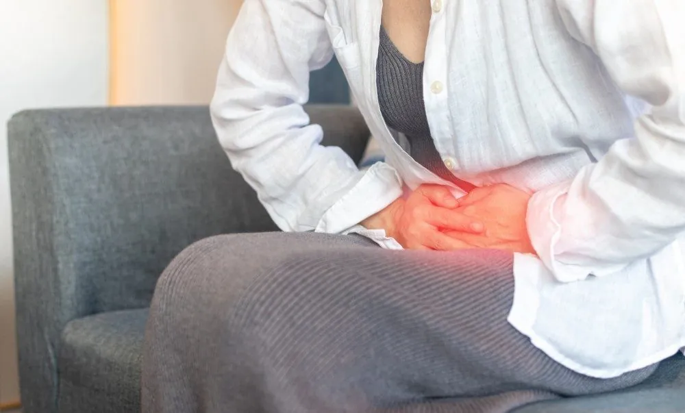 A woman on a sofa holding her lower abdomen in pain
