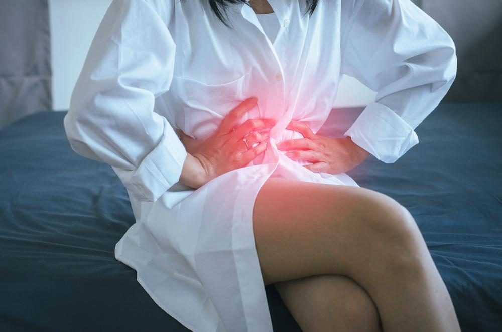 A woman sitting on a bed, holding her lower abdomen in pain