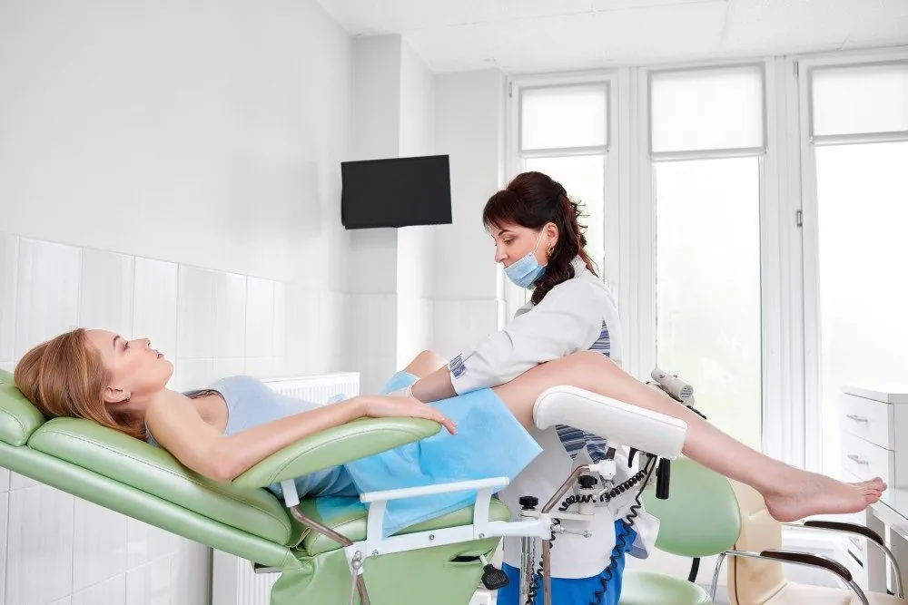 A patient on an exam chair while a clinician prepares for a colposcopy