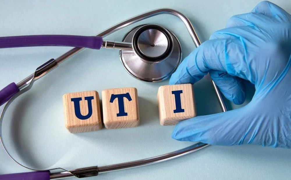 Wooden blocks spelling UTI next to a stethoscope and a gloved hand